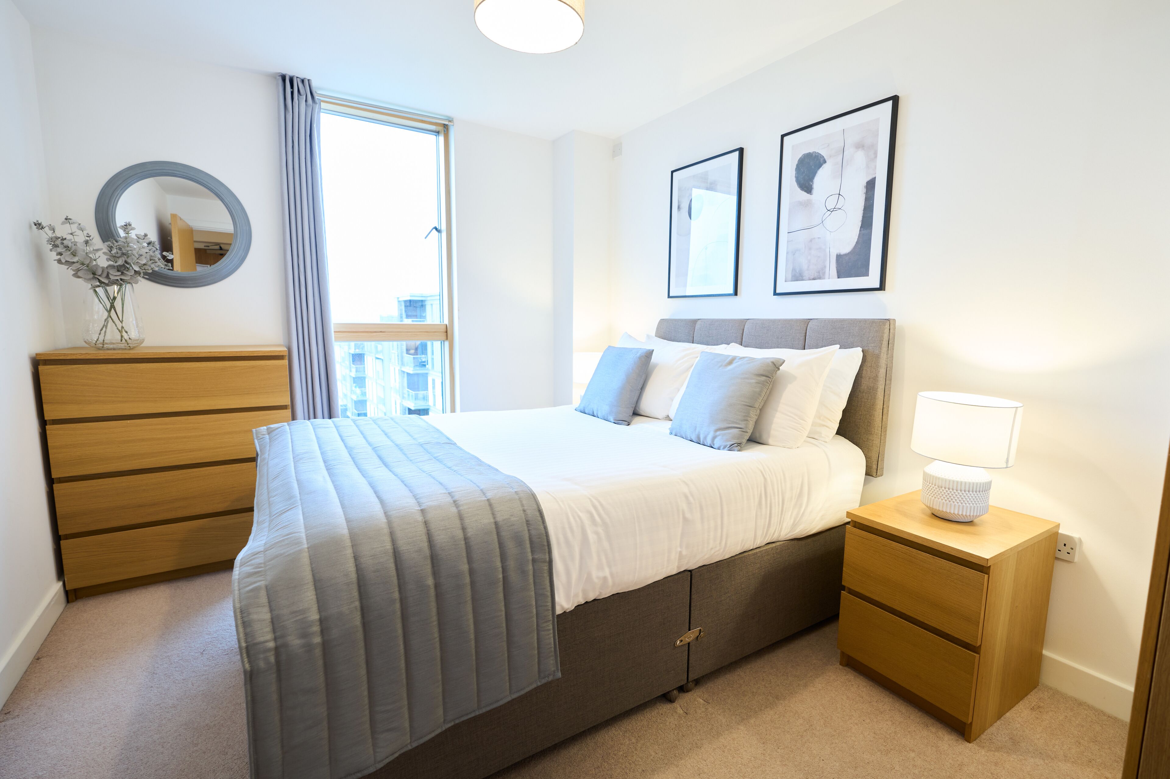 A neatly arranged bedroom with a bed, bedside tables, a dresser, and a window with curtains.