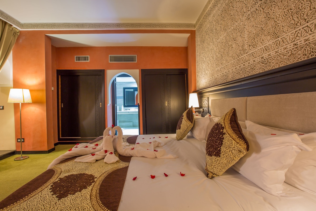 A hotel room with a bed, pillows, a carpet, and a view of the outside.