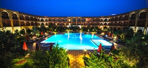 A large outdoor swimming pool surrounded by lounge chairs and umbrellas, with a building featuring arched balconies in the background. - Ennakhil Marrakech Hotel & SPA (Marrakech)