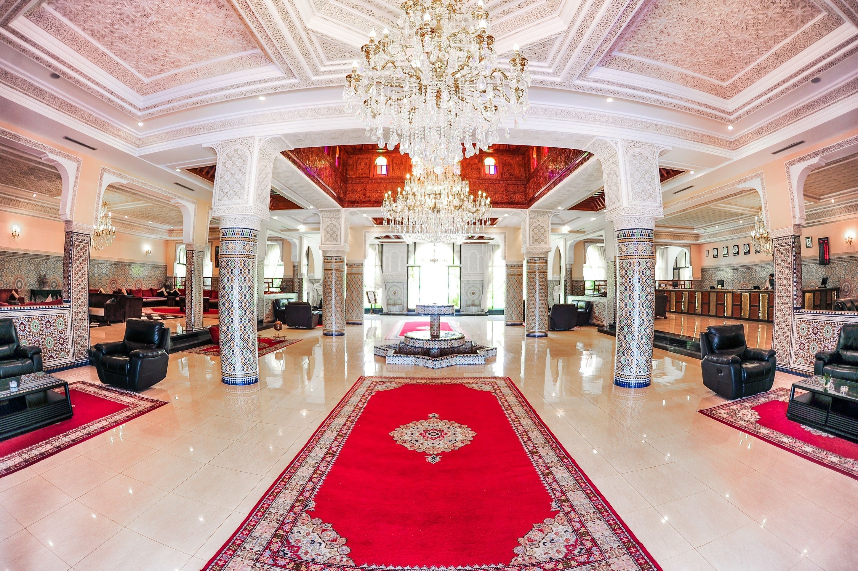 Un'imponente hall con tappeto rosso, colonne decorate e un grande lampadario.