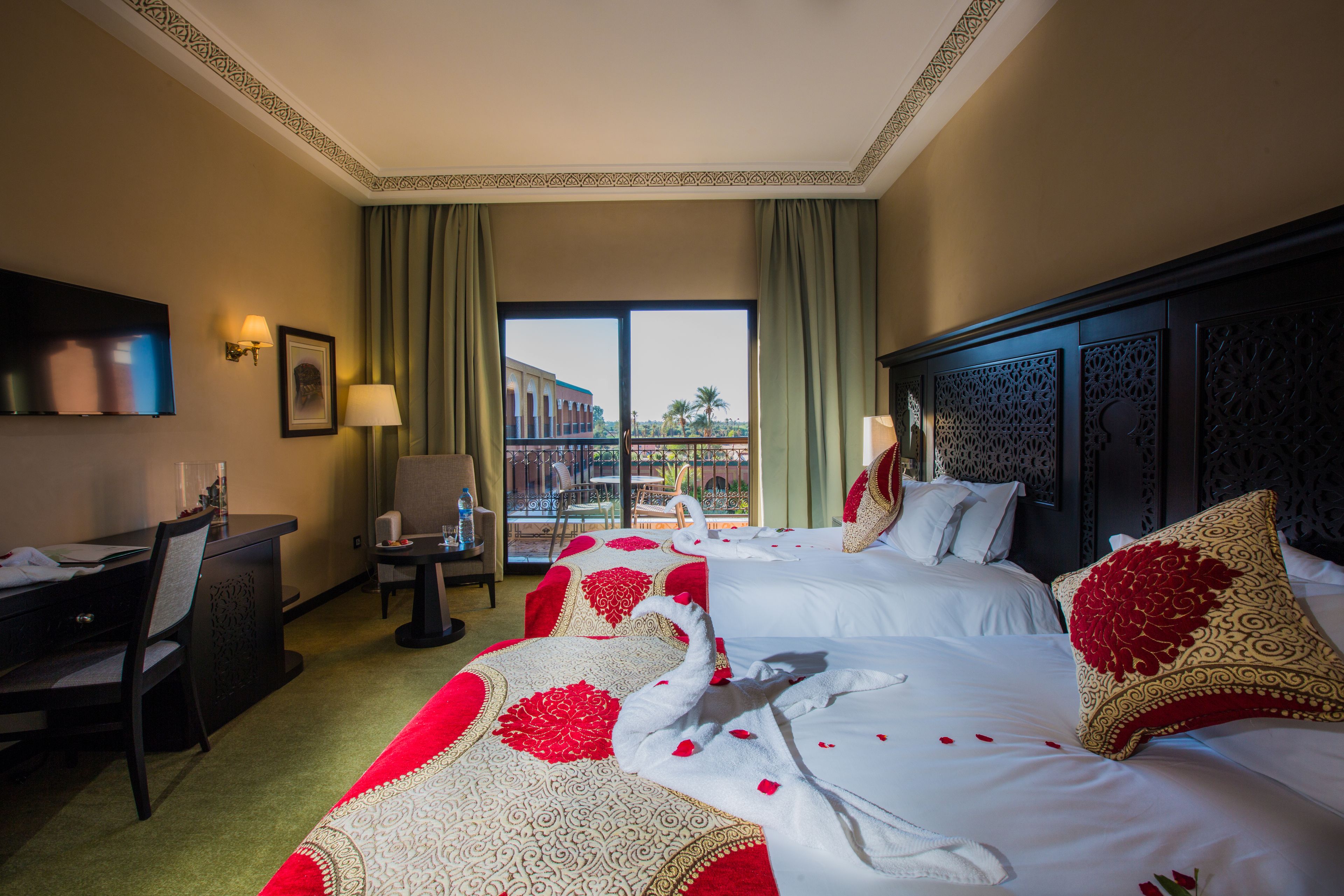 A hotel room with two beds, a desk, a chair, and a balcony with a view.