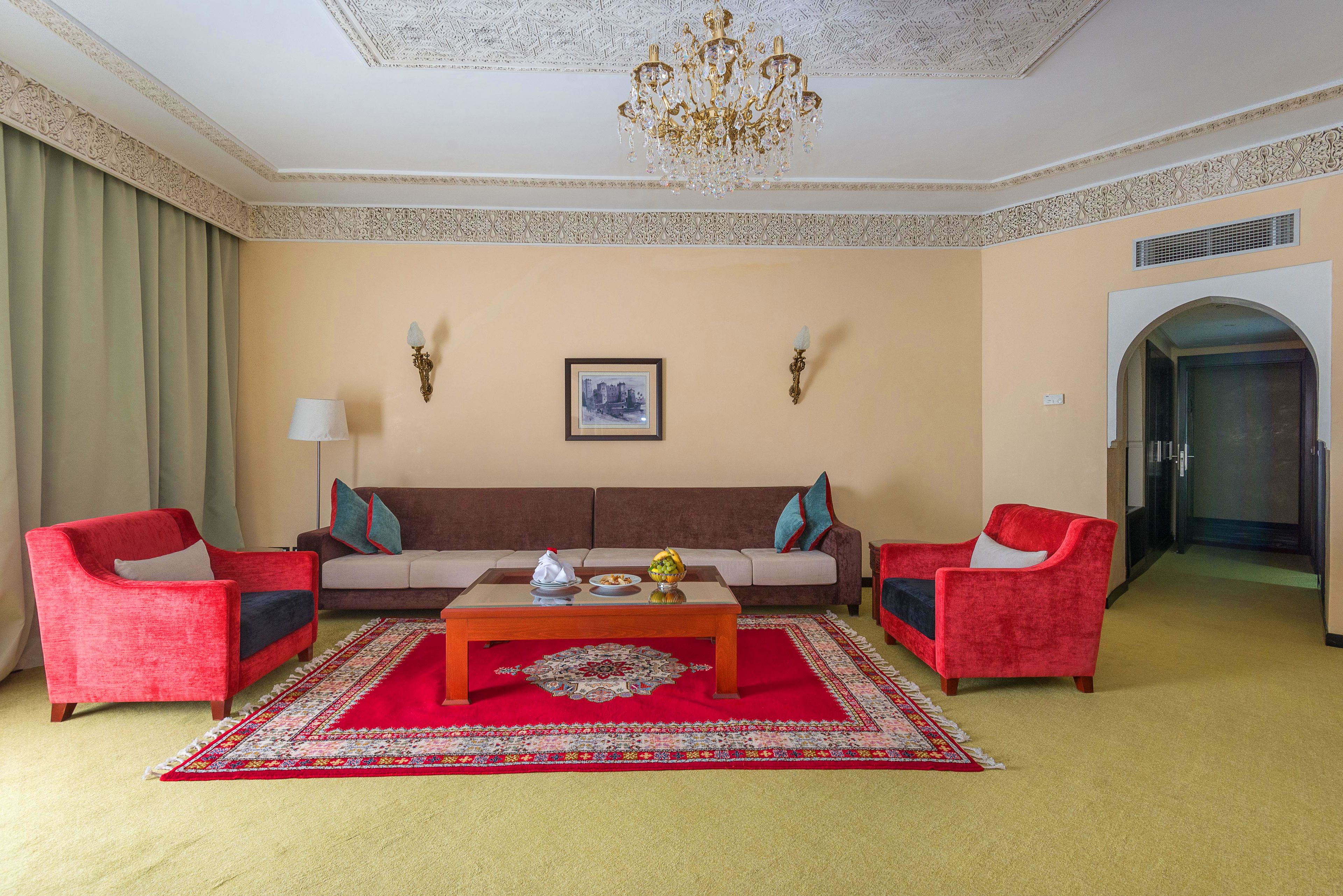 A living room with a beige sofa, red armchairs, a coffee table, and a chandelier.