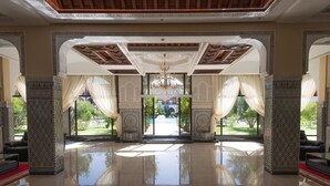 A spacious lobby with ornate columns, a chandelier, and large windows offering a view of the outdoor area. - Ennakhil Marrakech Hotel & SPA (Marrakech)