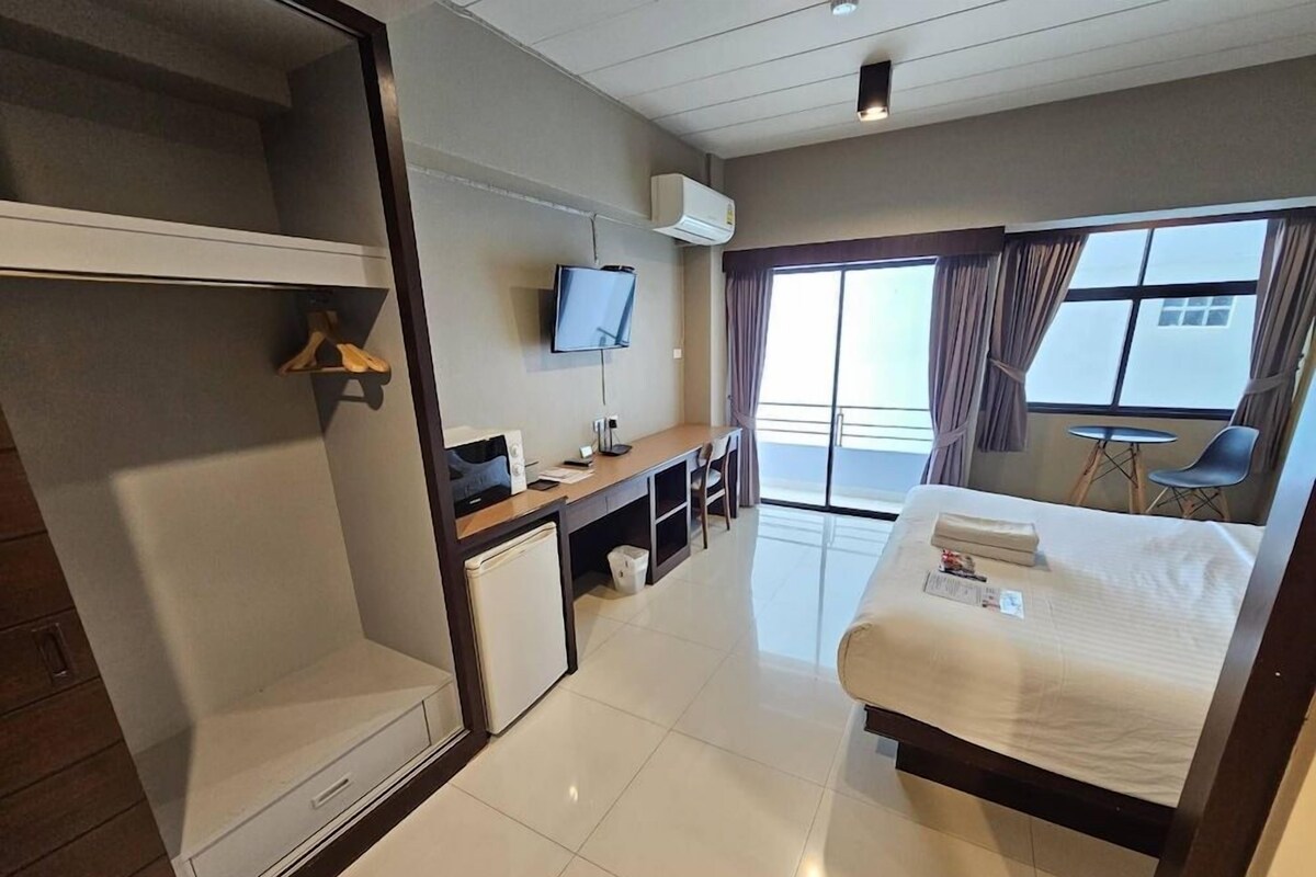 Une chambre d’hôtel avec un lit, un bureau, une télévision et un balcon offrant une vue.