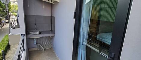 A narrow balcony with a sliding glass door, a small sink, and a utility box.