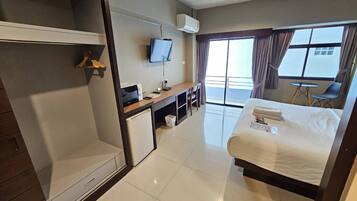 A hotel room with a bed, a desk with a computer, a TV, a mini-fridge, and a balcony with a view.