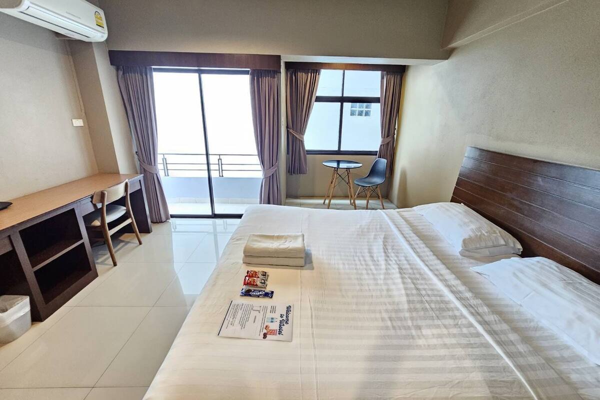 Une chambre d’hôtel avec un lit, un bureau, une chaise et une petite table. Il y a une fenêtre avec des rideaux et une vue sur l’extérieur.