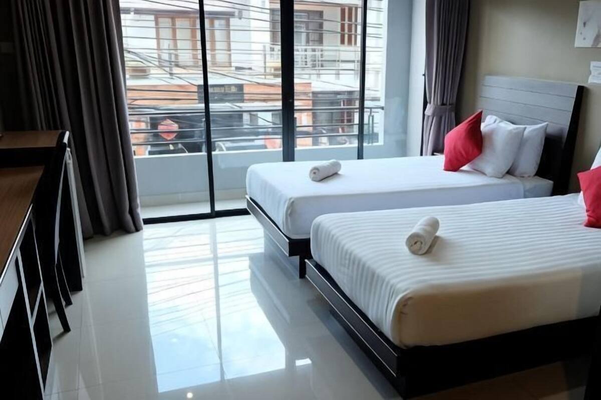 Une chambre d’hôtel avec deux lits, un bureau et une vue sur la ville grâce à de grandes fenêtres.