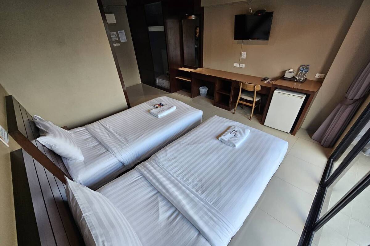 Une chambre d’hôtel avec deux lits simples, un bureau, une télévision et une fenêtre.
