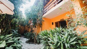 Une cour avec un chemin en pierre, entourée d’une végétation luxuriante et d’un bâtiment orange doté d’un balcon.