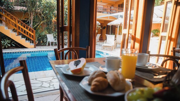 Une table de petit-déjeuner avec vue sur la piscine, comprenant une table avec des croissants, des fruits et du jus, ainsi qu’une chaise.