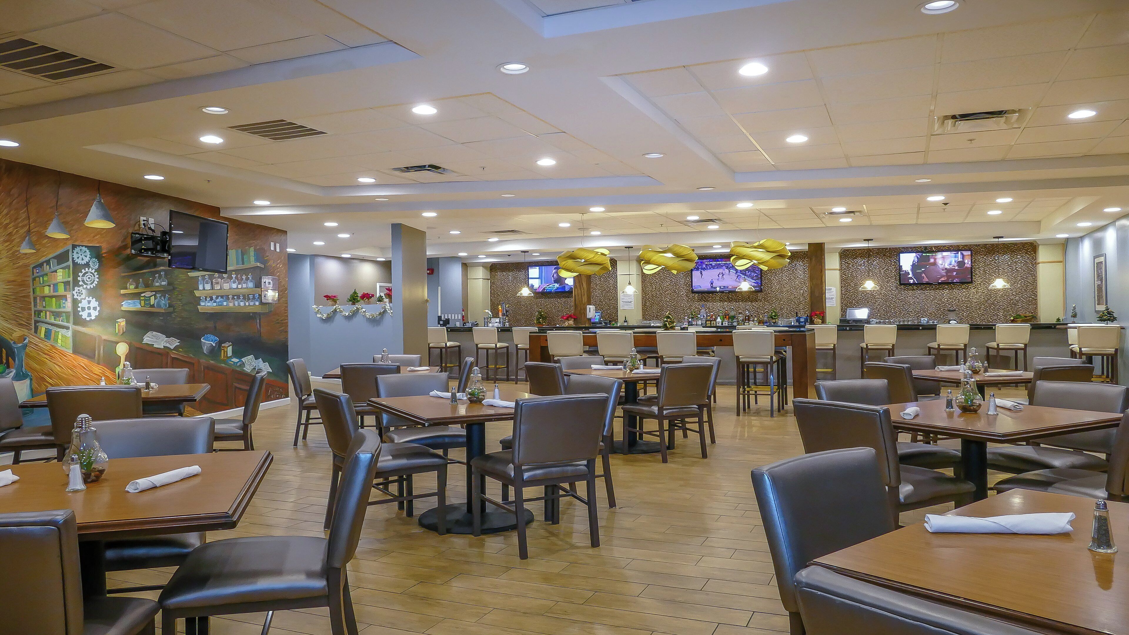 Un restaurante con varias mesas y sillas, una zona de bar y una pantalla de televisión en la pared.