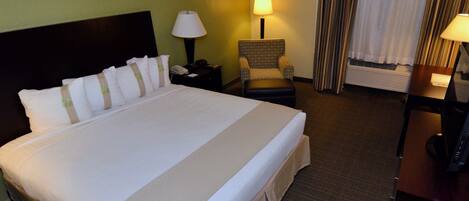 A hotel room with a large bed, a chair, a desk, and a lamp.