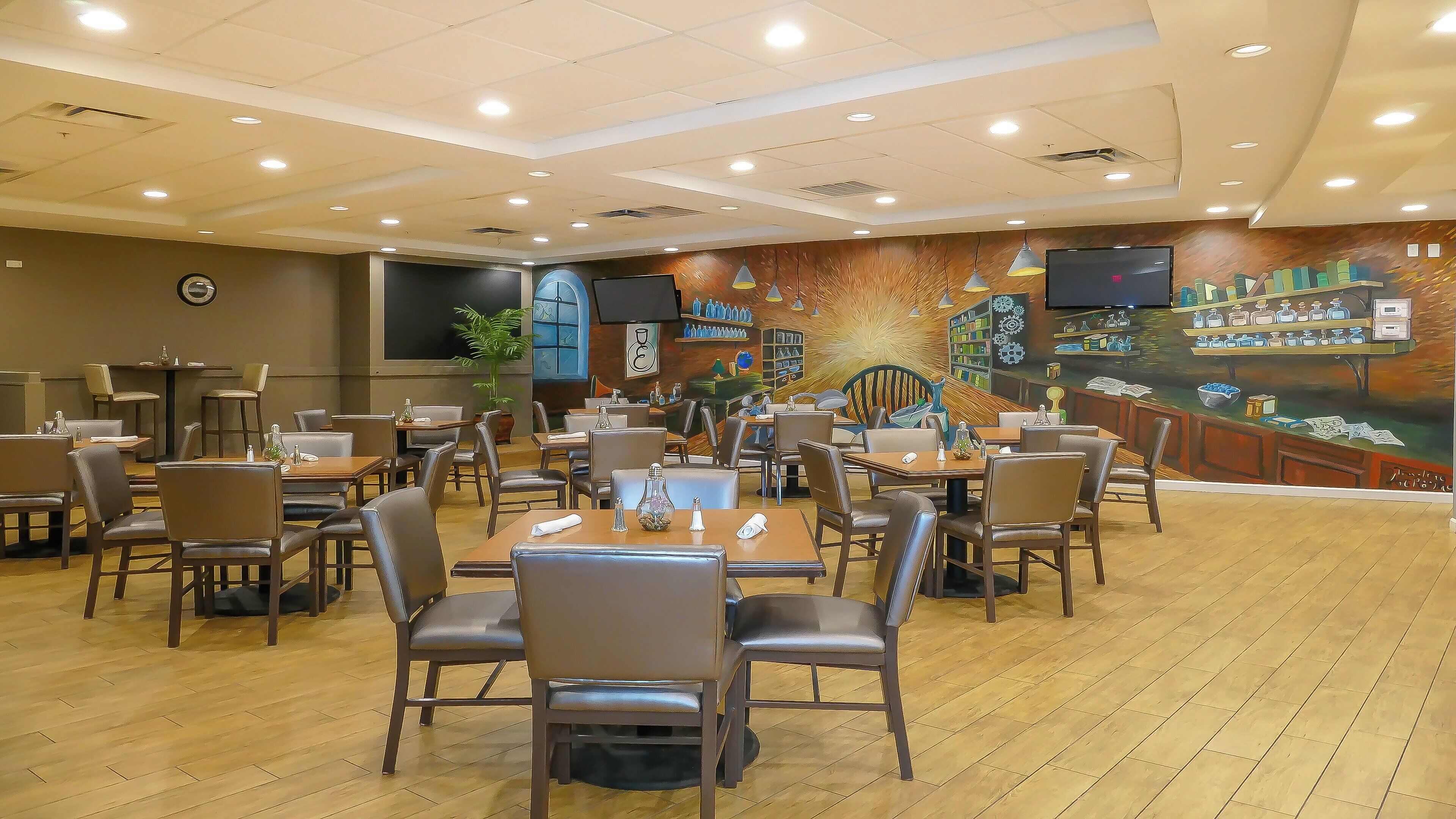 A restaurant with multiple tables and chairs, a large mural on the wall, and ceiling lights.