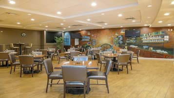 A restaurant with multiple tables and chairs, a large mural on the wall, and ceiling lights.