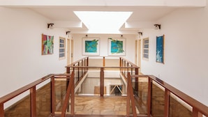 Un interior amplio con una escalera central, paredes blancas y obras de arte en las paredes.