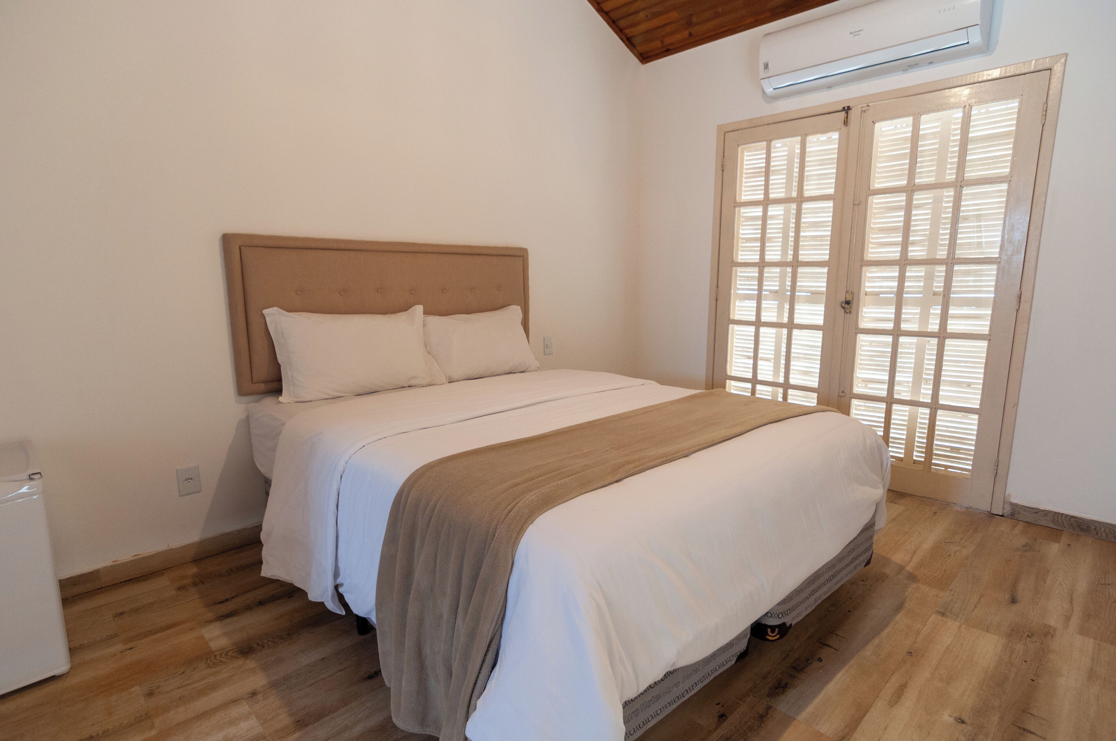A bedroom with a bed, a wooden floor, a white wall, and a window with blinds.