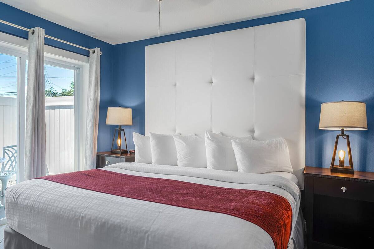 A bedroom with a large bed, two bedside tables with lamps, a window with curtains, and a view of the outdoors.