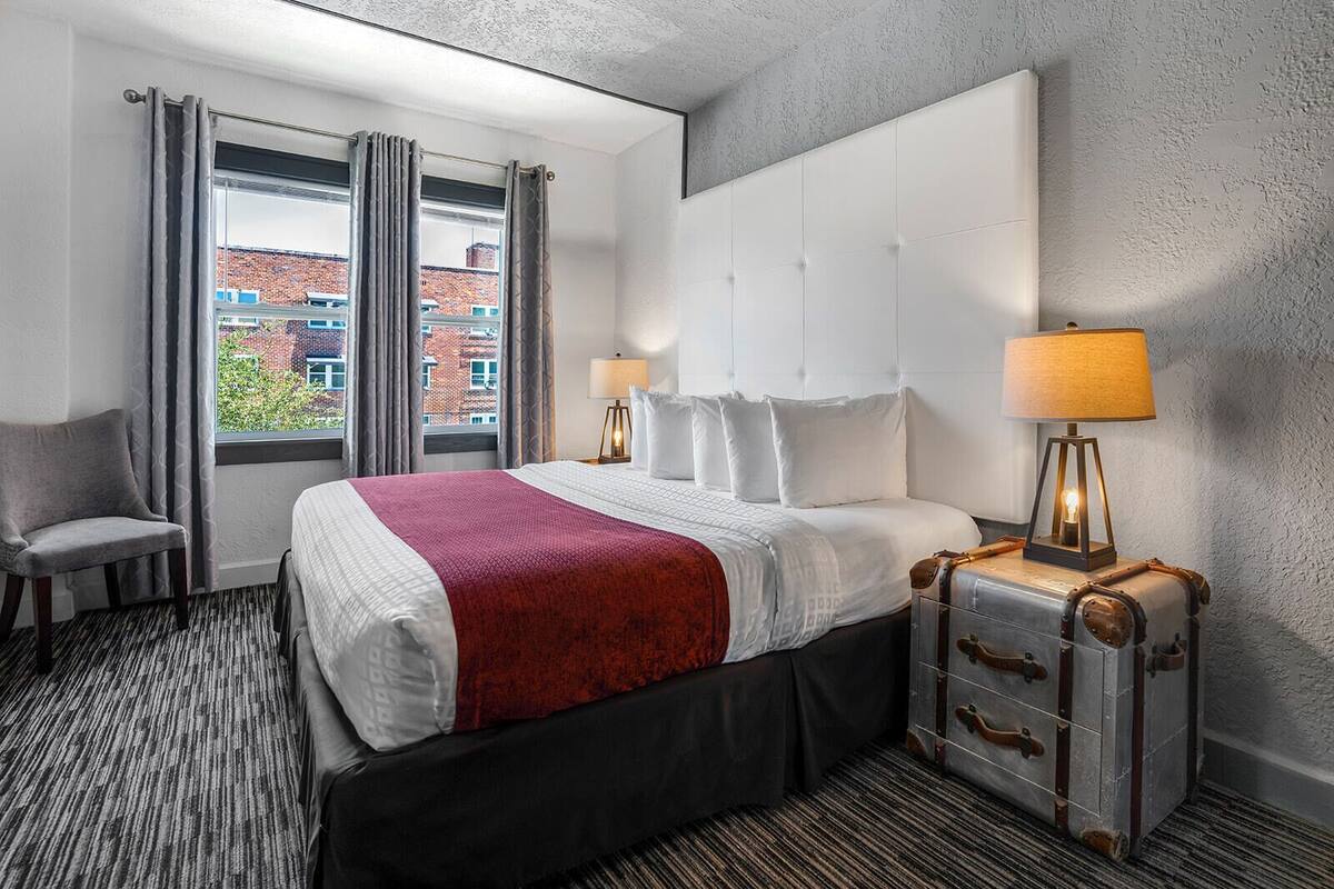 A hotel room with a large bed, two bedside lamps, a chair, and a suitcase.