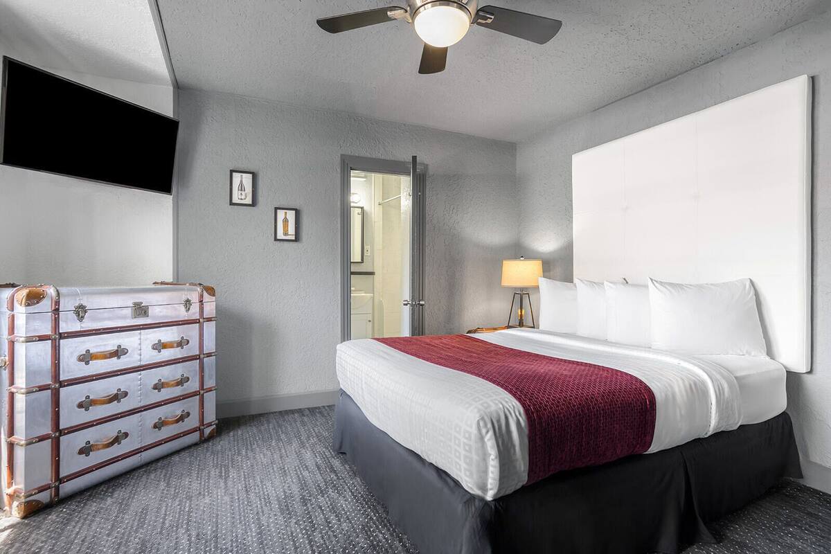 A hotel room with a bed, a dresser, a ceiling fan, and a door leading to a bathroom.