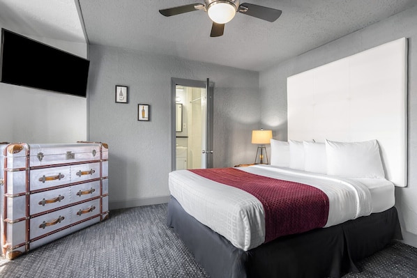 Habitación de hotel con cama, cómoda, ventilador de techo y puerta que da a un baño.