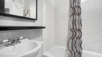 A bathroom with a white sink, a mirror, a bathtub, and a shower curtain with a geometric pattern.