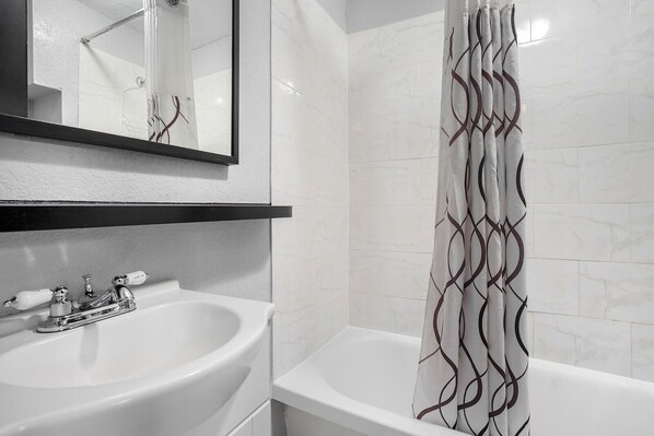 Une salle de bain avec un lavabo blanc, un miroir, une baignoire et un rideau de douche à motifs géométriques.