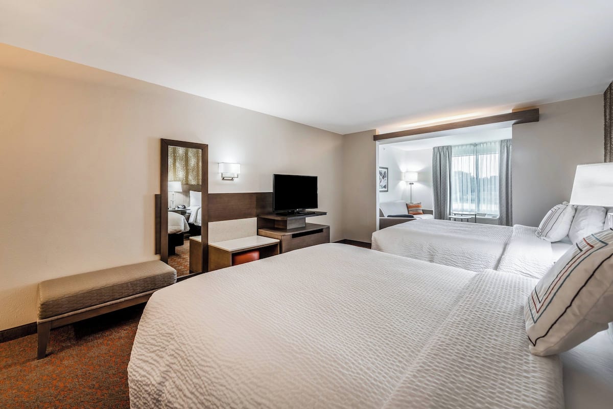 Habitación de hotel con dos camas, un escritorio, un televisor de pantalla plana, un banco y un ventanal con cortinas.