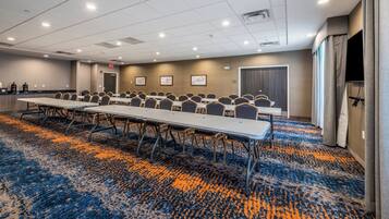 A conference room with long tables and chairs, a patterned carpet, and a ceiling with recessed lighting.