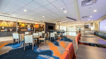 Een ruime hotel lobby met verschillende zithoeken, een receptiebalie en een groot scherm met informatie.
