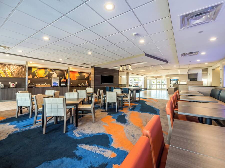 Een ruime hotel lobby met verschillende zithoeken, een receptiebalie en een groot scherm met informatie.