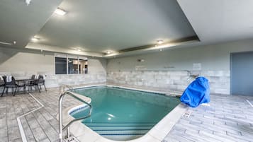 An indoor swimming pool with a tiled floor, a pool ladder, and a covered area.