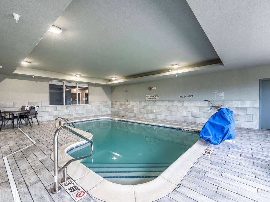 An indoor swimming pool with a tiled floor, a pool ladder, and a covered area.
