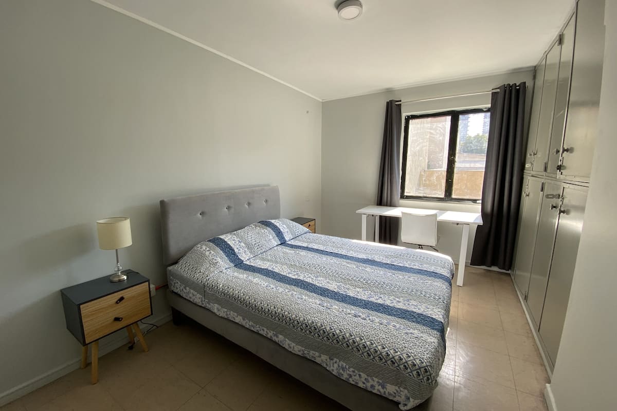Un dormitorio con cama, mesita de noche, lámpara, escritorio y armario.
