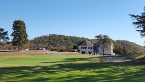 En golfbana med ett klubbhus, en flagga och en parkeringsplats med bilar.
