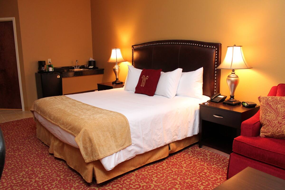 Une chambre d’hôtel avec un grand lit, deux tables de chevet, un fauteuil rouge et un petit bureau avec une lampe.