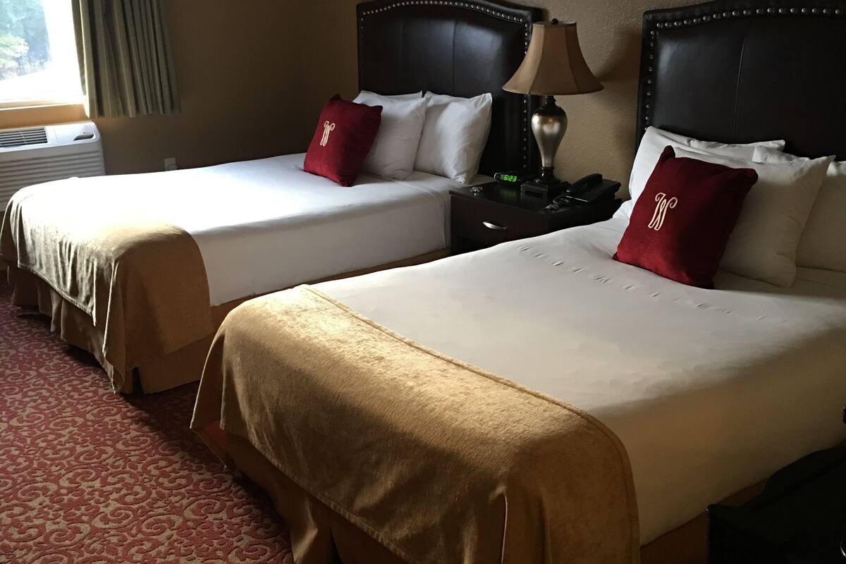 Une chambre d’hôtel avec deux lits, chacun doté d’une tête de lit, d’une table de chevet avec une lampe et d’un oreiller rouge.