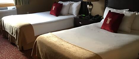 A hotel room with two beds, each with a headboard, a bedside table with a lamp, and a red pillow.