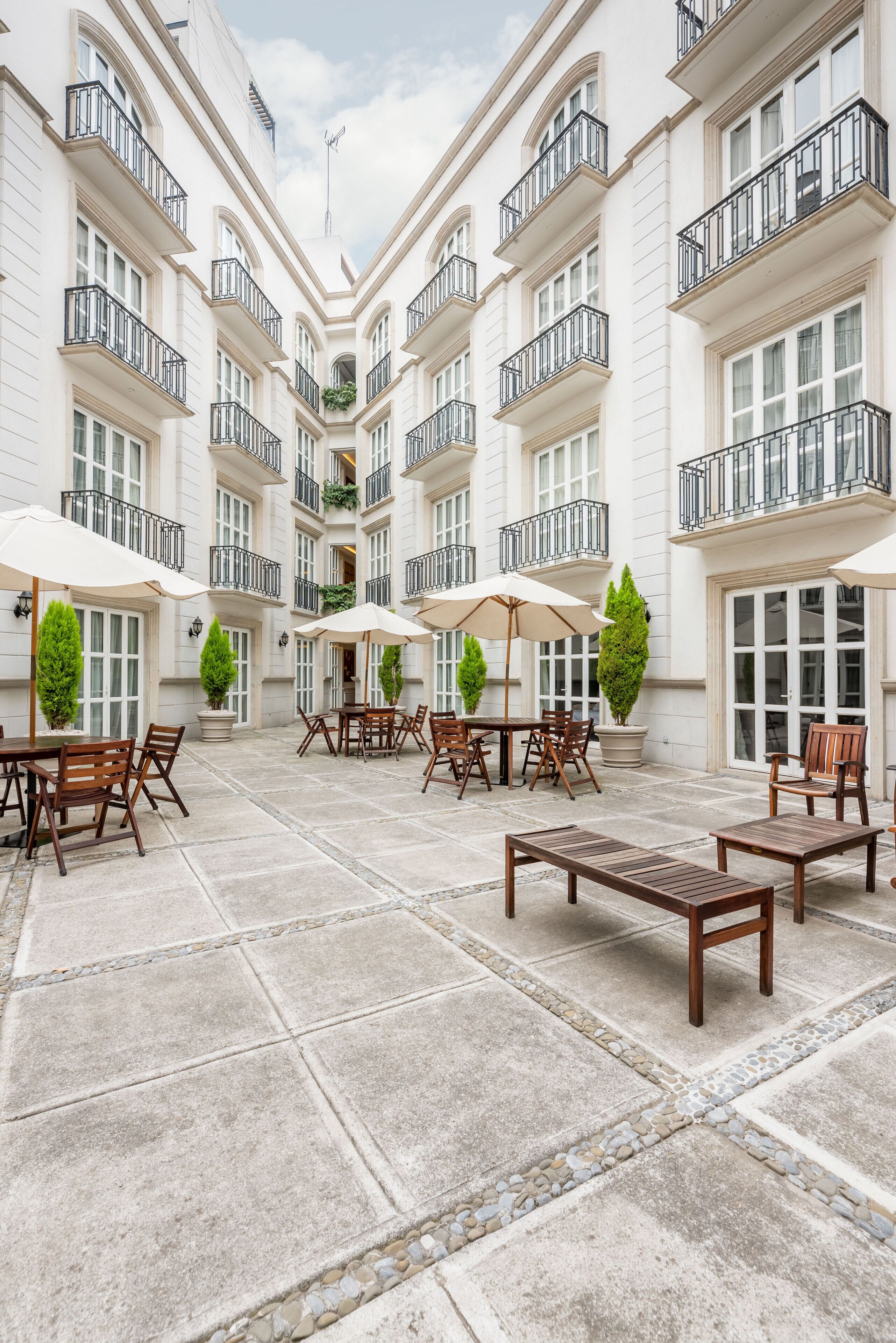 Un patio con mobiliario exterior, plantas en macetas y una fuente central.