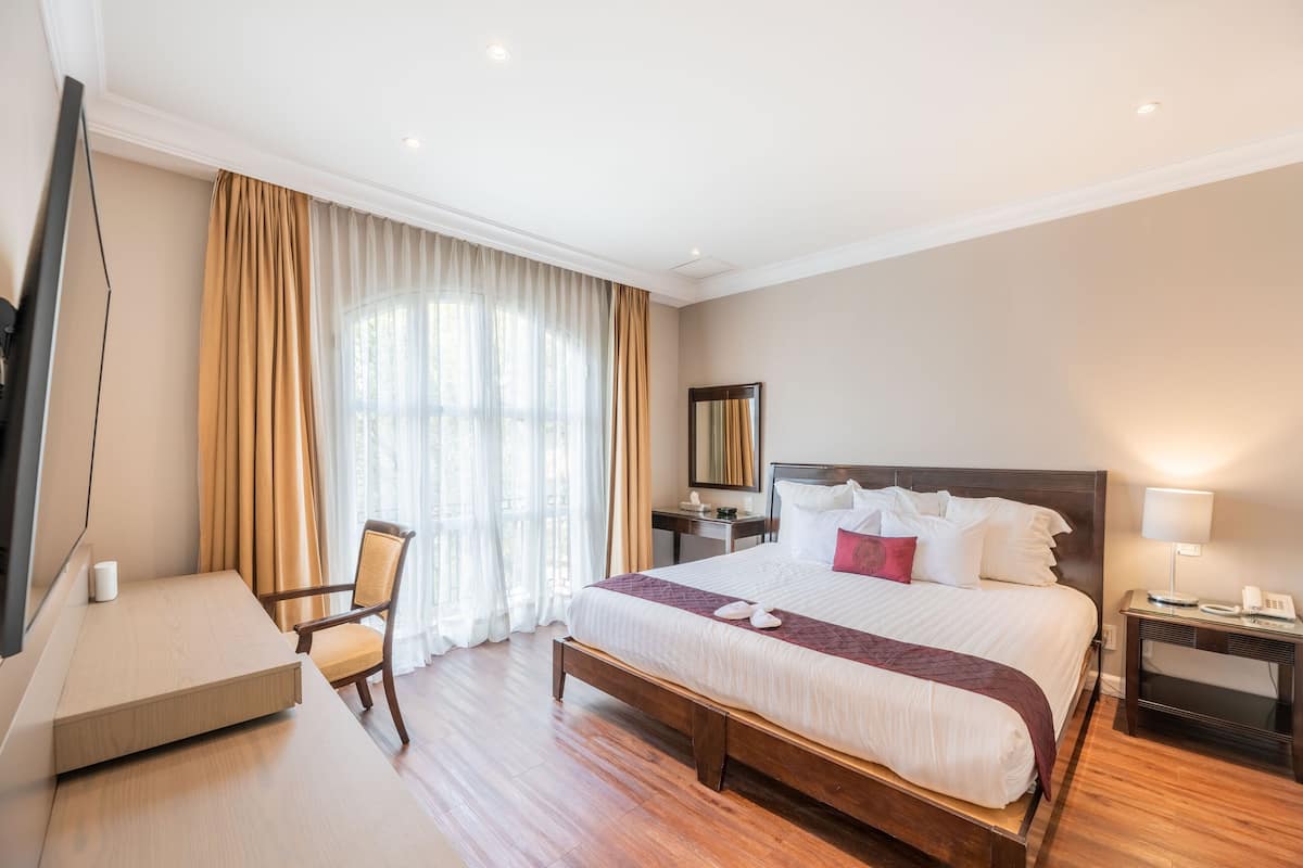 Een hotelkamer met een groot bed, een bureau, een stoel, een nachtkastje en een spiegel.