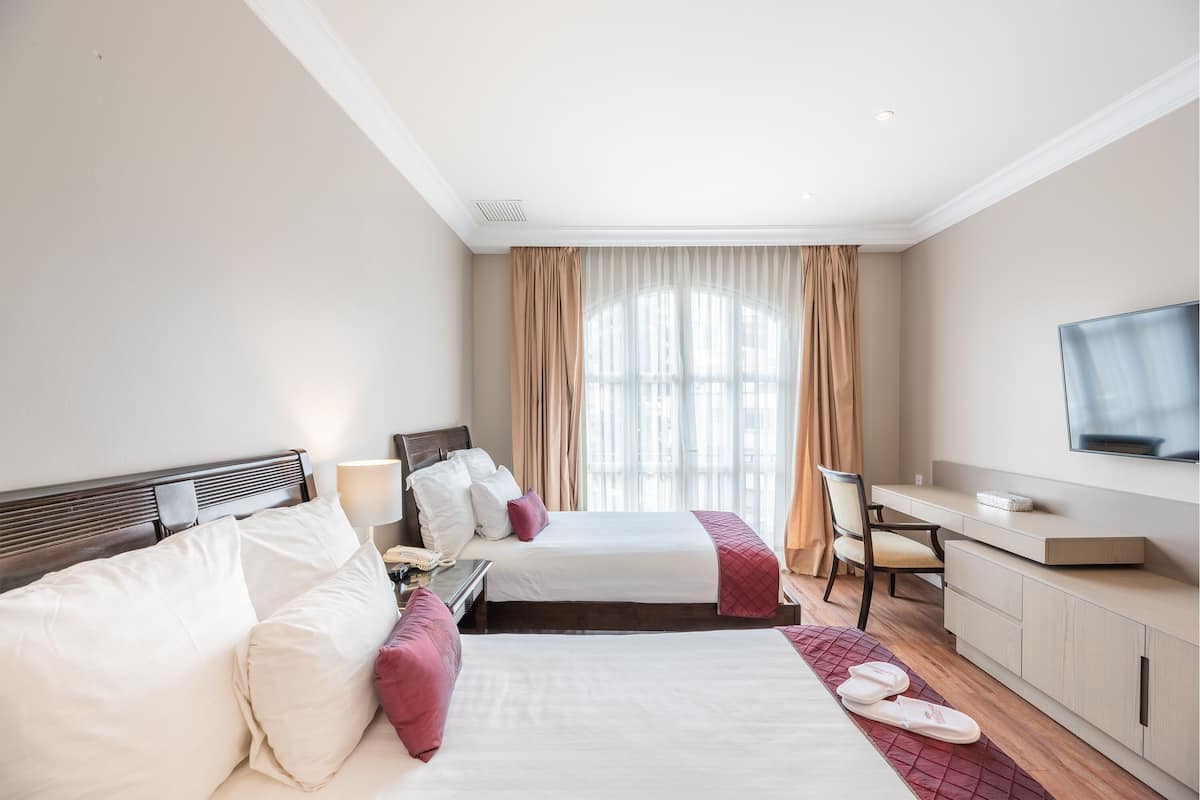 Een hotelkamer met twee bedden, een bureau, een stoel, een televisie en een raam met gordijnen.