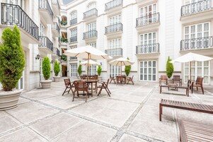 Un patio con mobiliario exterior, plantas en macetas y fachada de edificio con balcones.