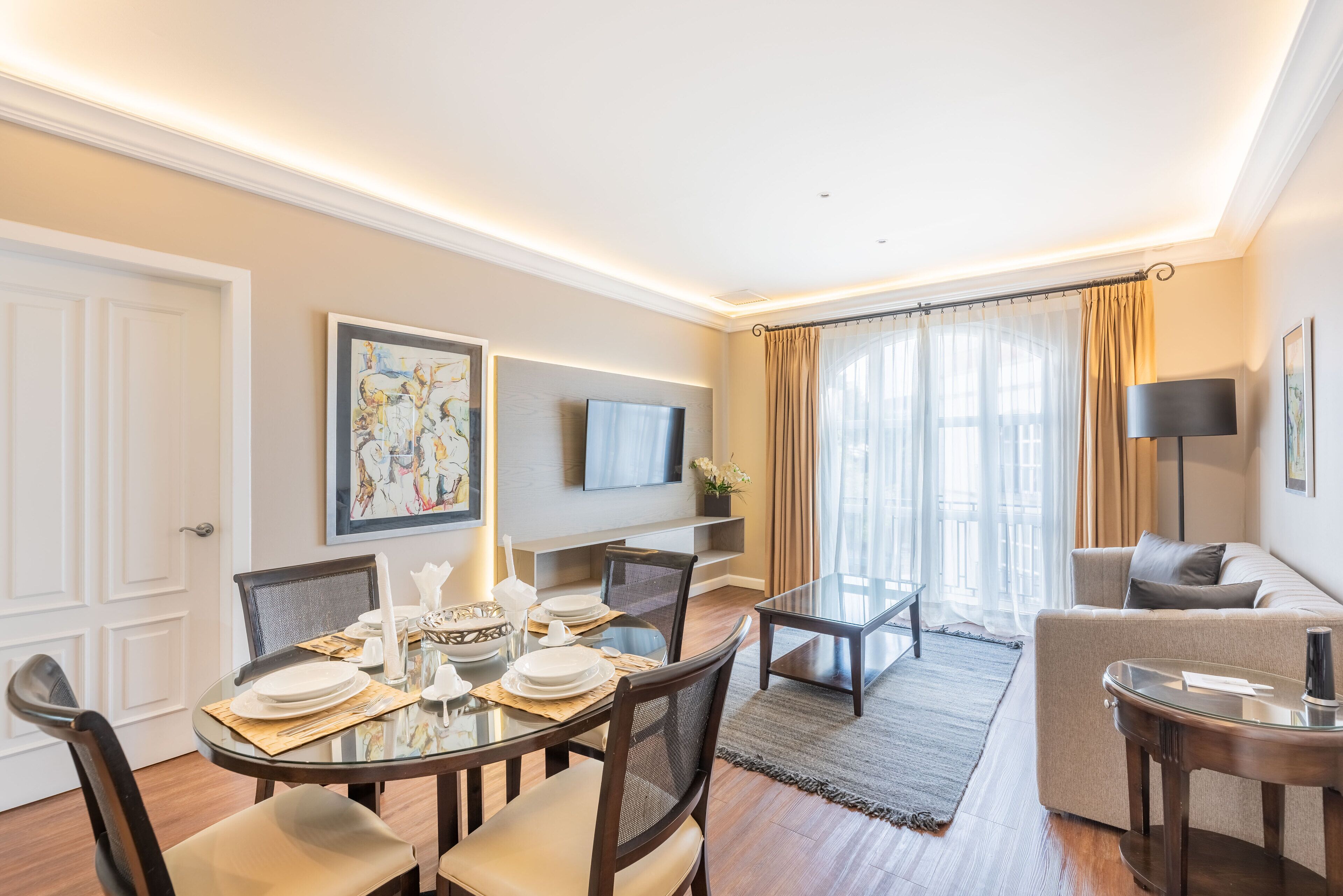 A modern living room with a dining area, a flat-screen TV mounted on the wall, and a sofa.