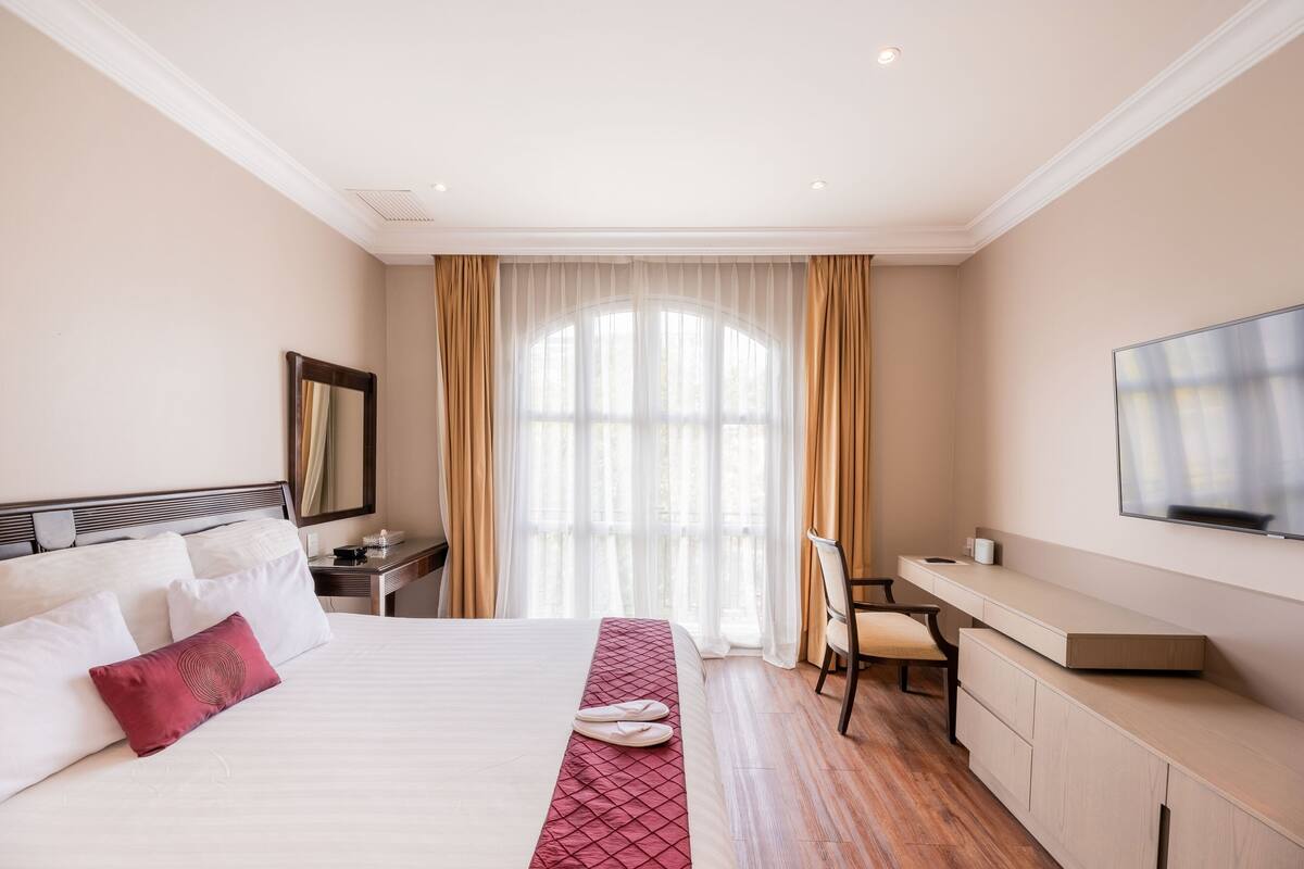 Een hotelkamer met een groot bed, een bureau, een stoel en een aan de muur bevestigde televisie.