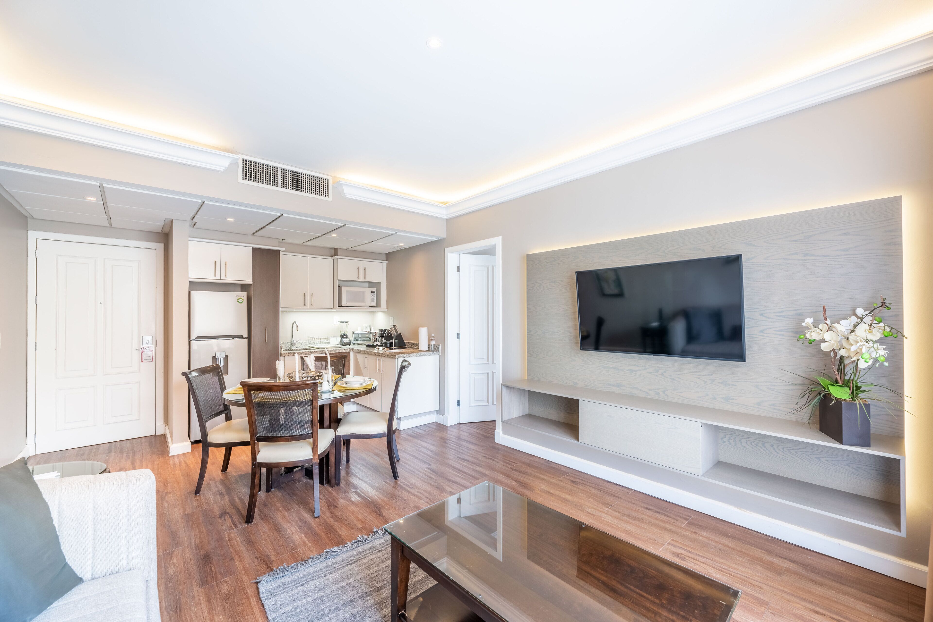 A modern living room with a flat-screen TV, dining area, and kitchen.