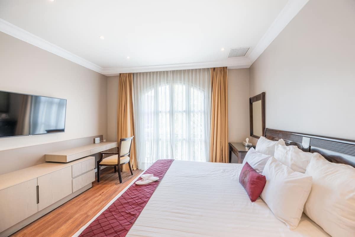 Een hotelkamer met een groot bed, een bureau met stoel, een aan de muur bevestigde televisie en een raam met gordijnen.