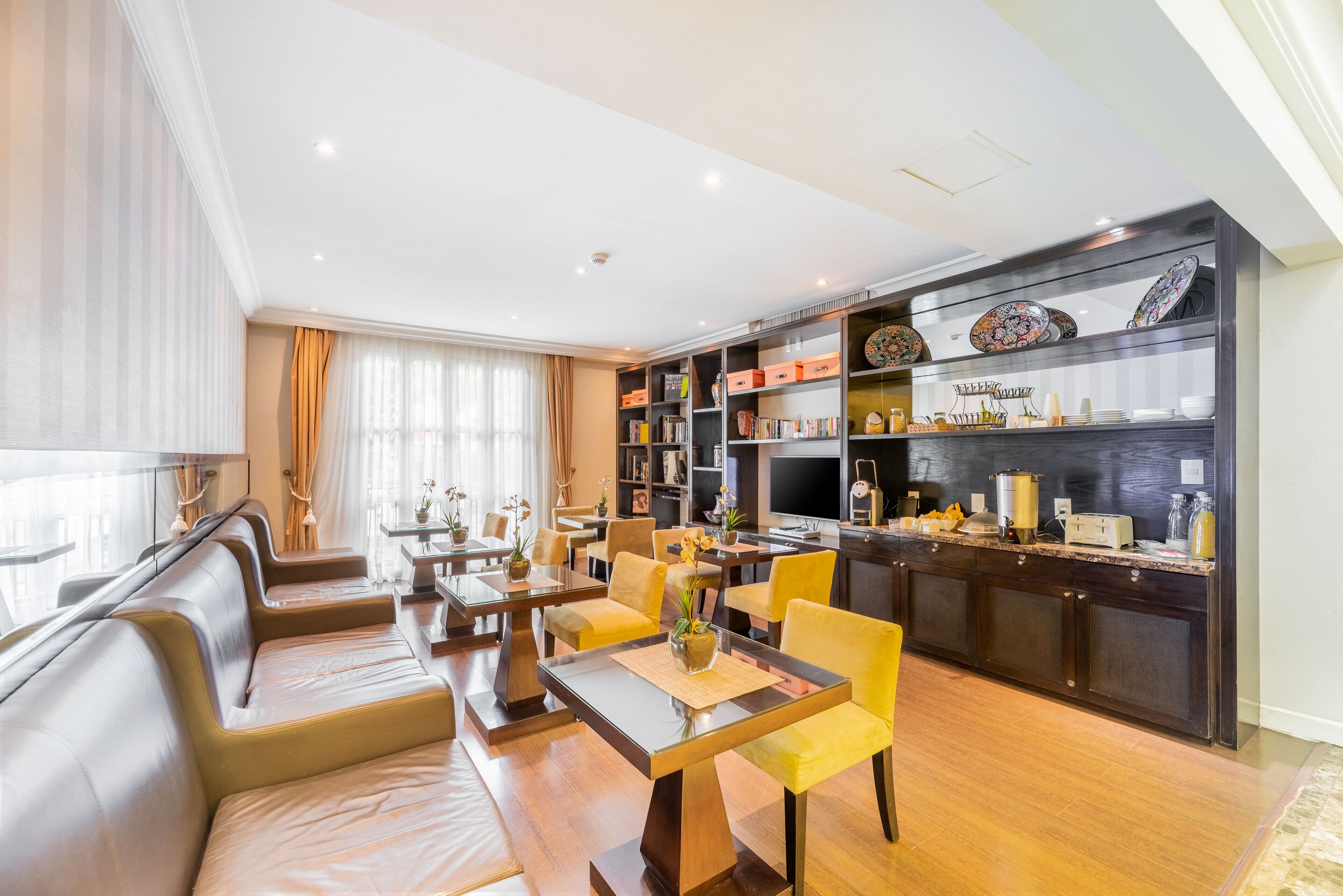 A modern hotel lobby with a dining area, seating, and a kitchen area with shelves.