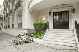 Un edificio con un cartel que dice “Grand Plano Residencial”, que presenta una escalera que lleva a la entrada, una fila de balcones y bicicletas estacionadas afuera.