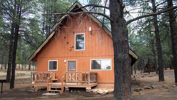 A wooden cabin with a porch, surrounded by trees.