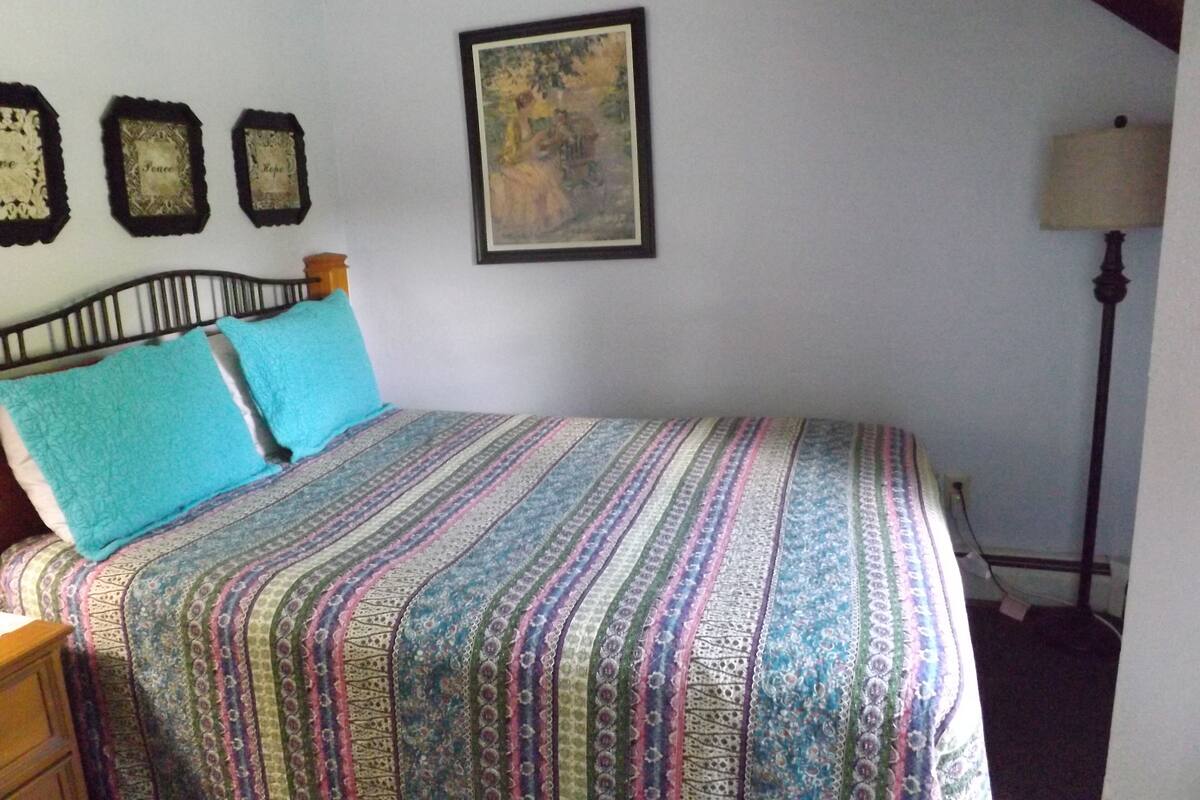 A bedroom with a bed, a nightstand, a lamp, and three wall-mounted clocks.